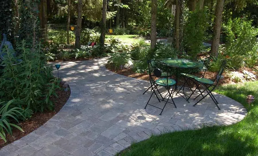 A shaded paver patio with a bistro set under mature trees