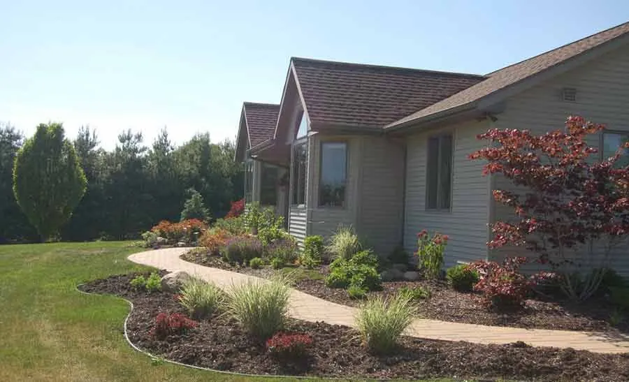 Curved foundation bed — A long, confidently curved bed line running the front of a ranch home with layered shrub planting.
