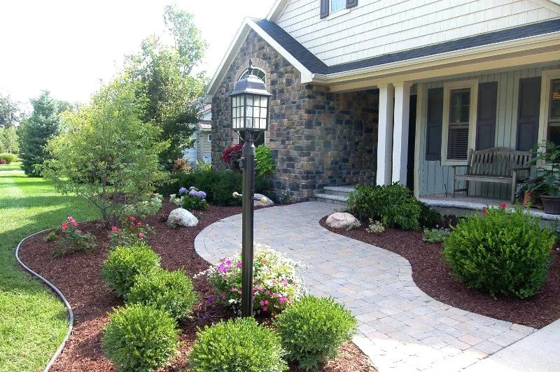 Curved paver walkway and mulched foundation beds at a stone-front home